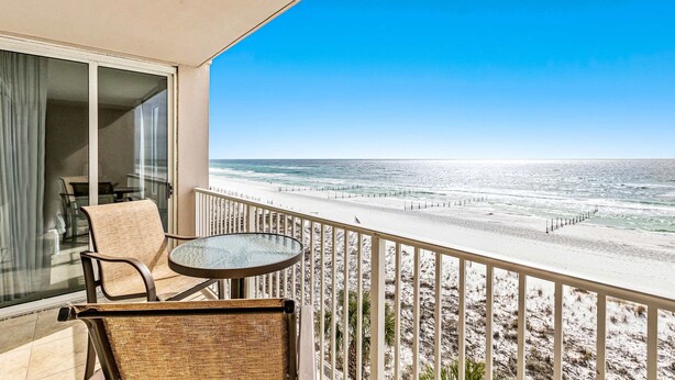 Een balkon met uitzicht op het strand, een tafel en twee stoelen.