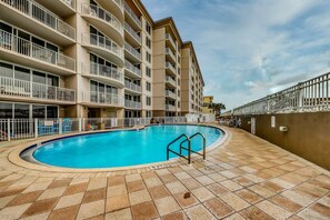 A swimming pool with a tiled deck, surrounded by a multi-story building with balconies. - Fifth floor oceanfront condo with pool, ocean view, W/D (Fort Walton Beach)