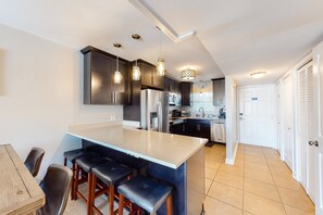 Uma cozinha moderna com armários escuros, uma ilha central com banquetas, eletrodomésticos de aço inoxidável e iluminação pendente.
