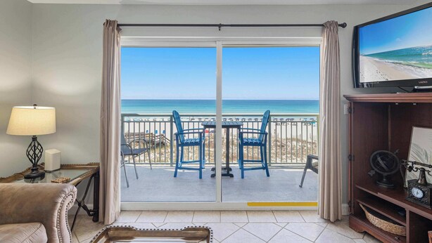 Een kamer met uitzicht op het strand, een televisie, een tafel met stoelen, een bank en een lamp.