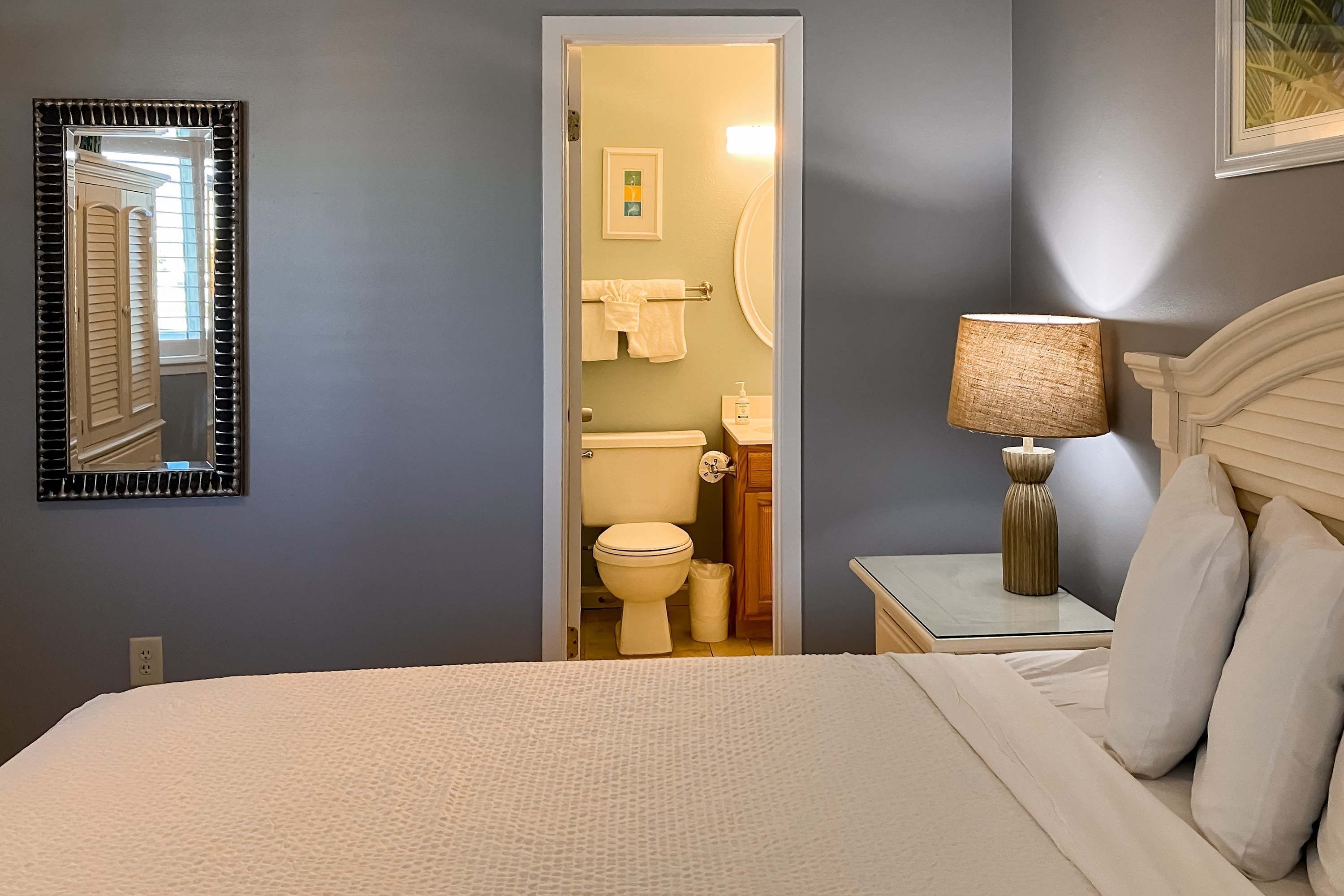 Une chambre à coucher avec un lit, une table de chevet avec une lampe, un miroir et une vue sur la salle de bain.