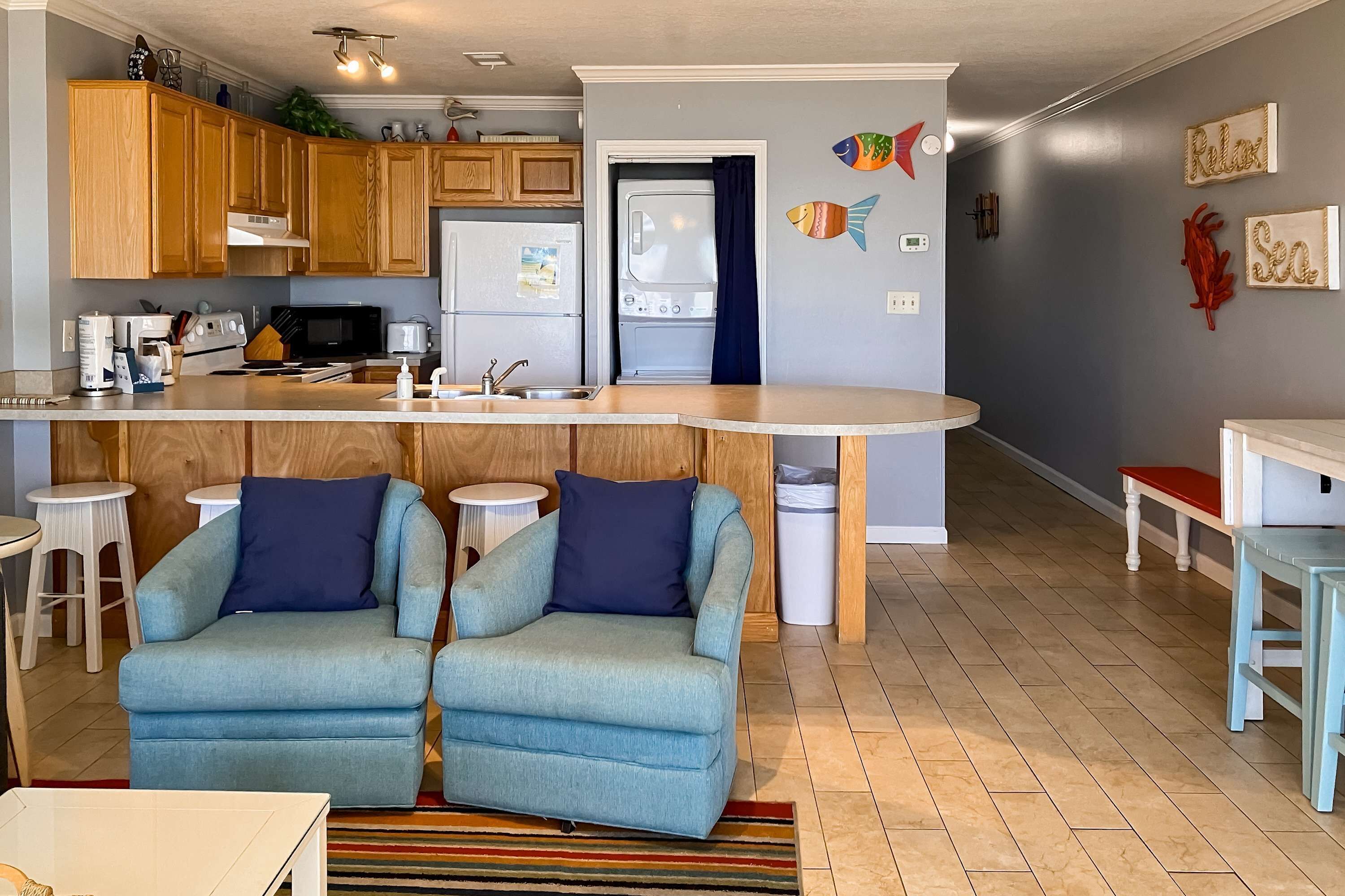 Une cuisine moderne avec des meubles en bois, un îlot central intégré et un coin salon avec deux fauteuils.