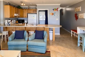 A modern kitchen with wooden cabinets, a built-in island, and a seating area with two armchairs. - 2nd Floor Gulf Front Condo with Gulf Views, Close To Entertainment (Fort Walton Beach)