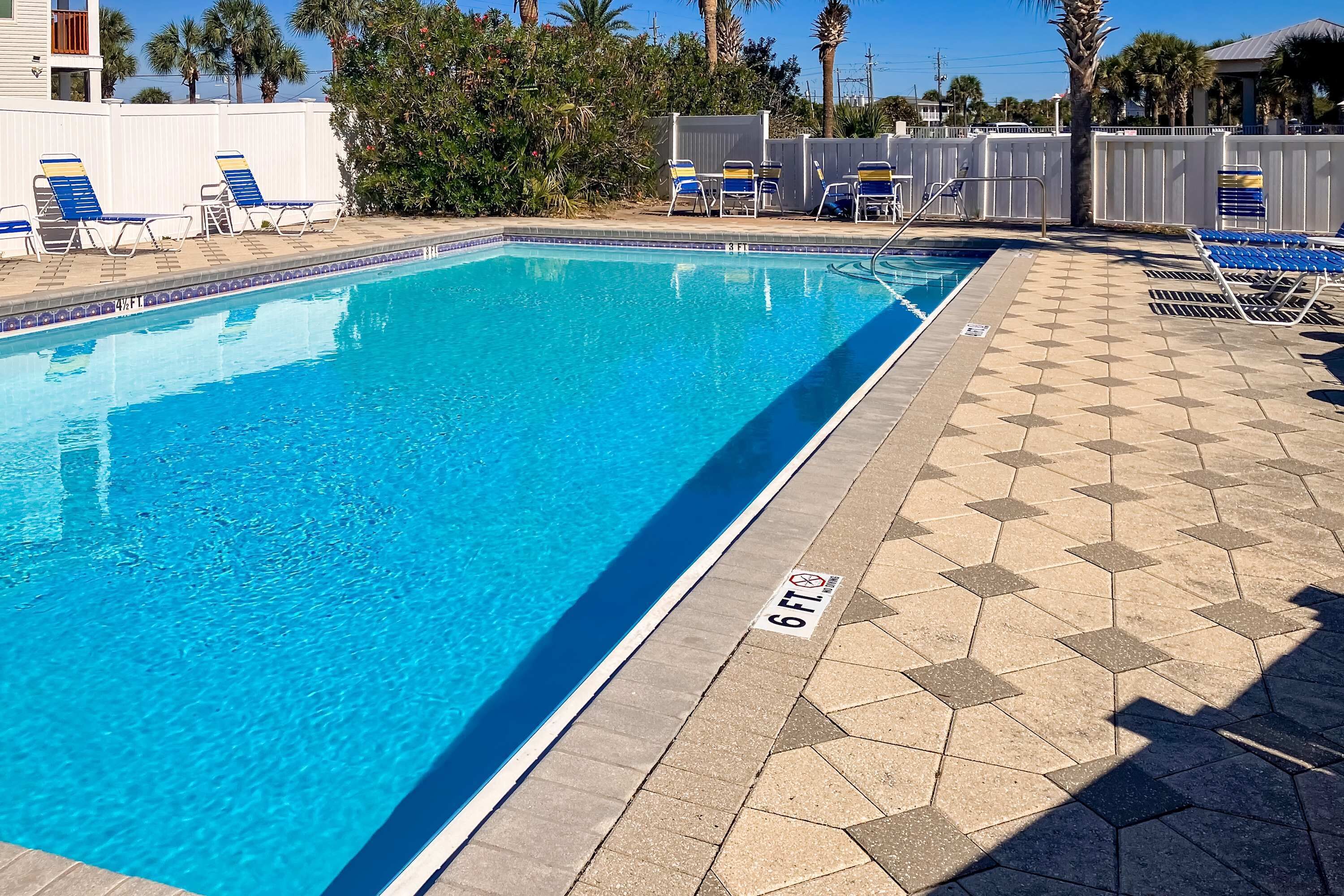 A swimming pool with a 6 ft depth marker, surrounded by lounge chairs and a tiled deck.