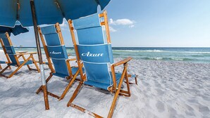 Strandstoelen onder een blauwe parasol met daarop de tekst 'Azure', geplaatst op een zandstrand met de oceaan op de achtergrond.