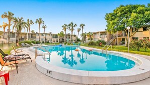 Ein Swimmingpool mit Liegestühlen und Palmen, umgeben von Mehrfamilienhäusern.