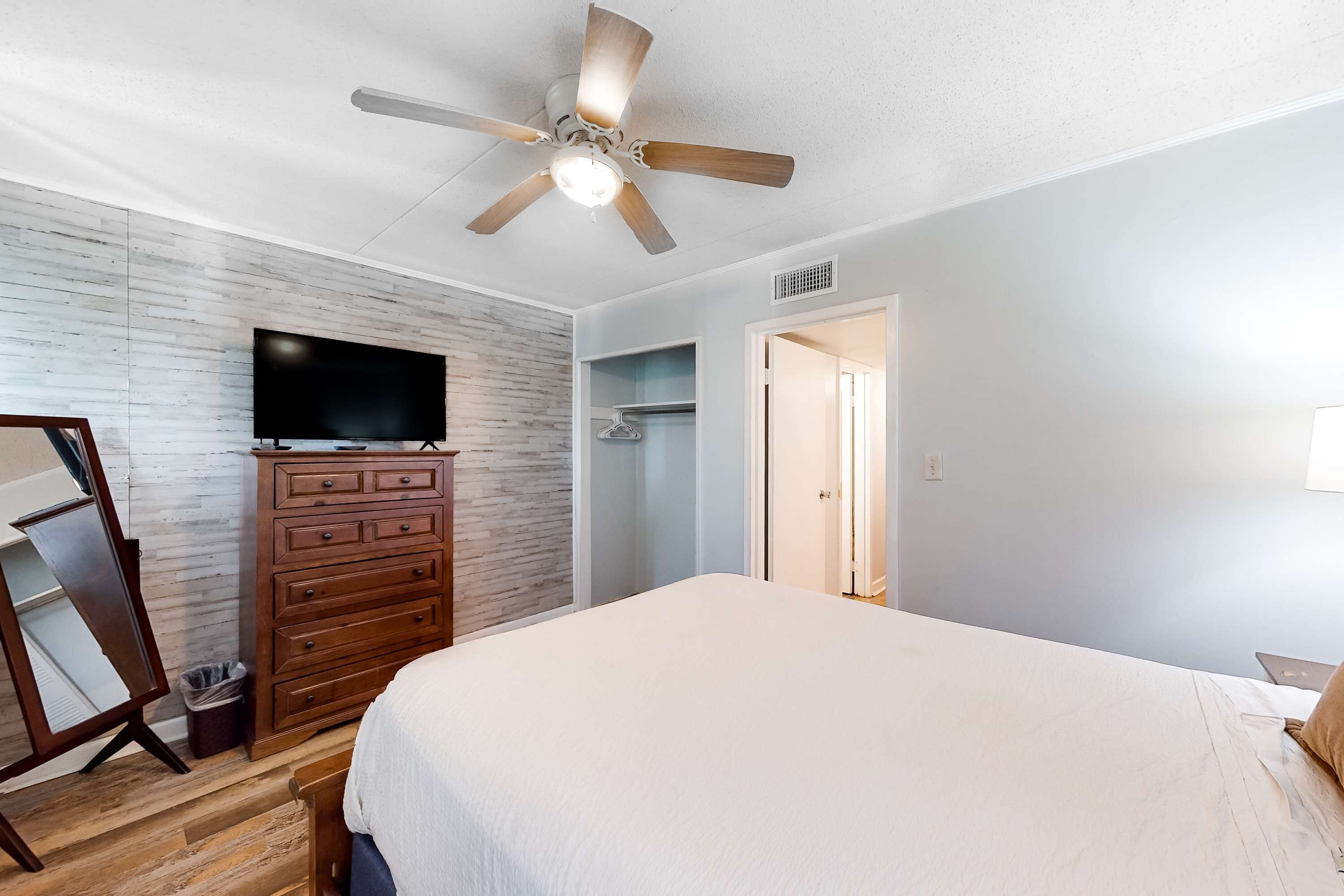 A bedroom with a bed, wooden dresser, TV, and a ceiling fan.
