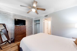A bedroom with a bed, wooden dresser, TV, and a ceiling fan. - Waterfront condo with pool, central AC, washer&dryer, and WiFi (Fort Walton Beach)