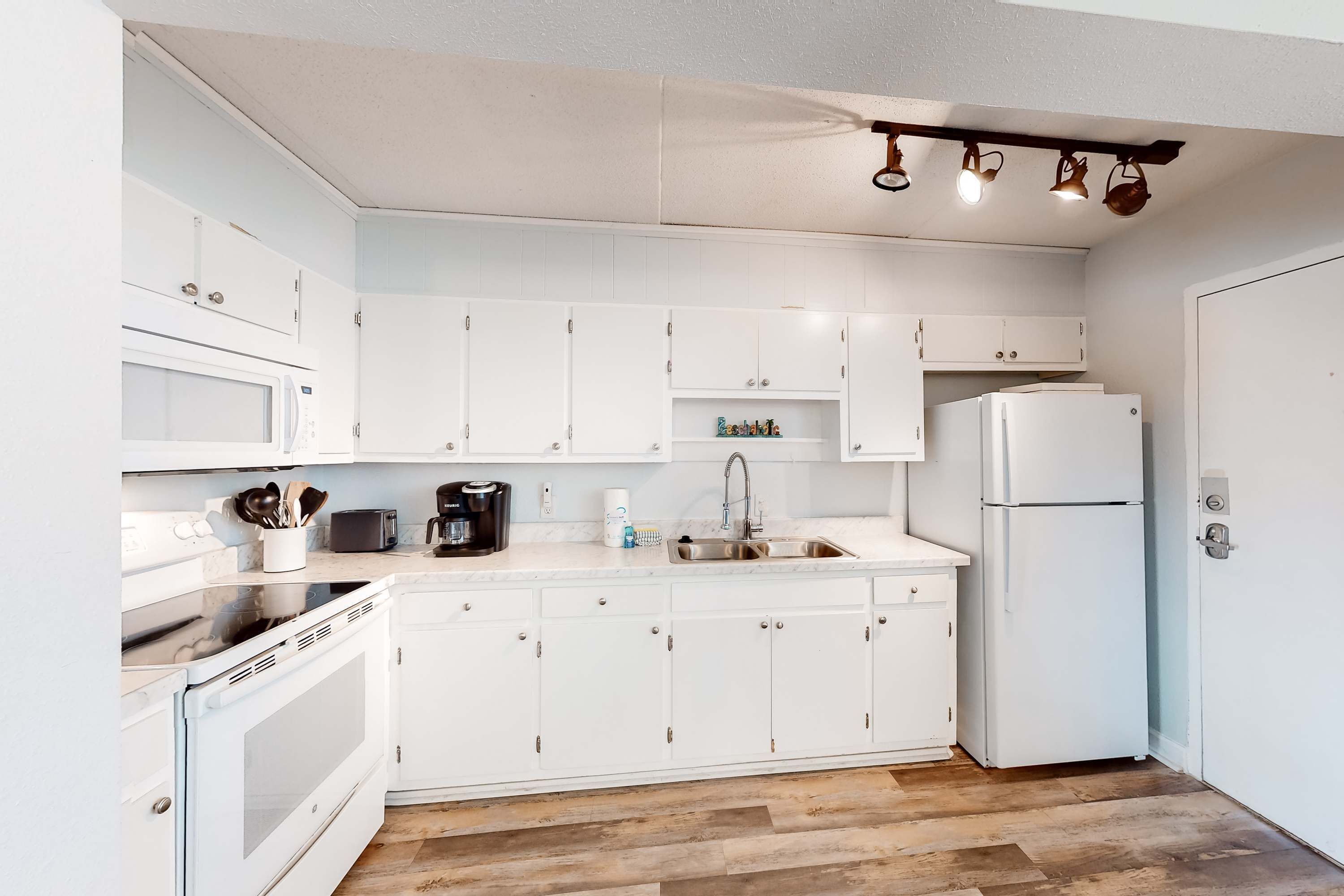 A modern kitchen with white cabinets, a stainless steel stove, a sink, and a refrigerator.