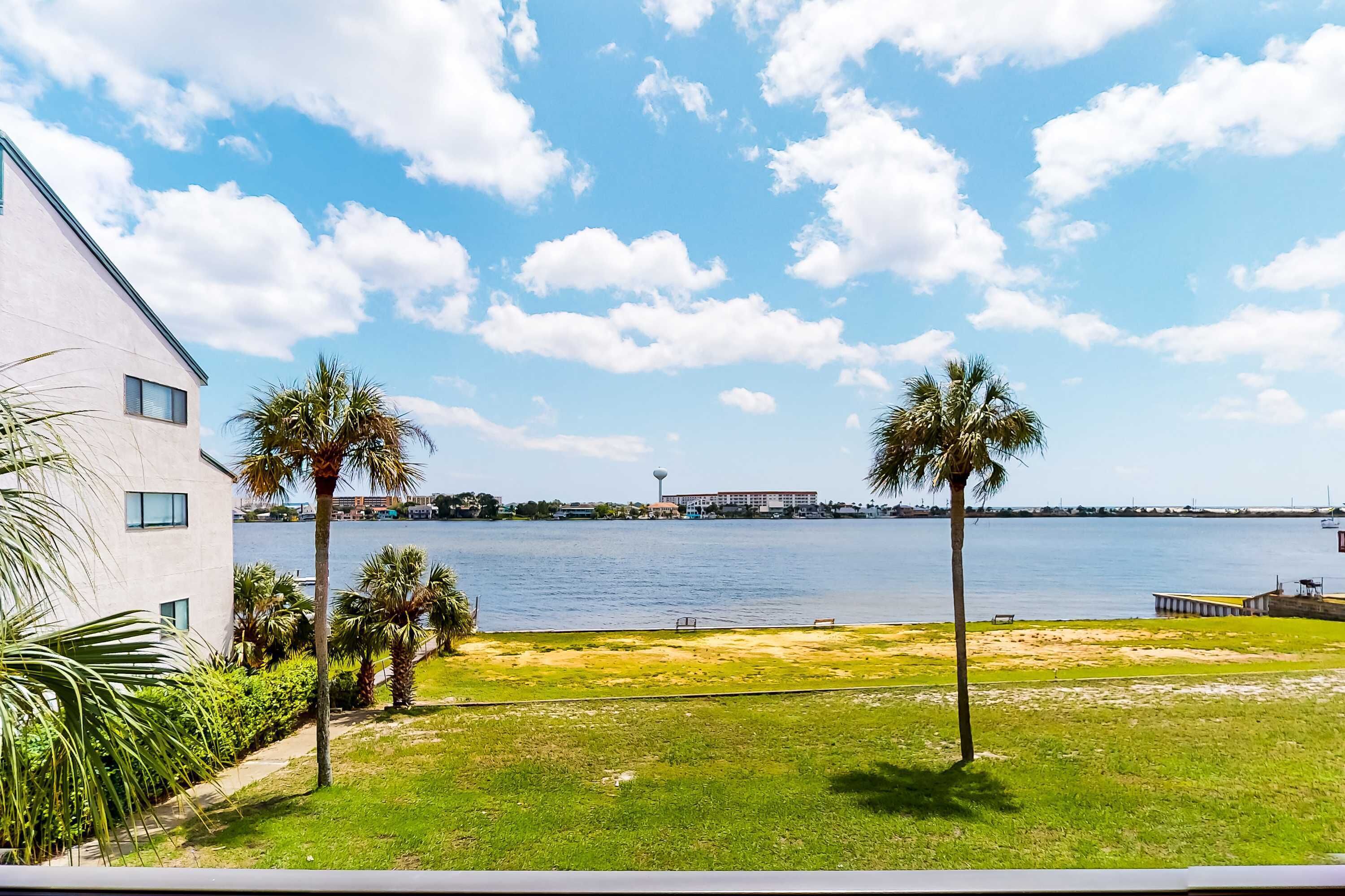 A view of a waterfront property with a grassy lawn, palm trees, and a building with large windows.