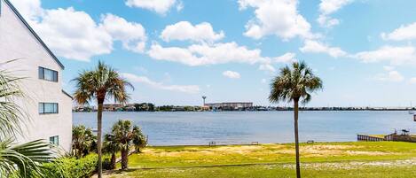 A view of a waterfront property with a grassy lawn, palm trees, and a building with large windows.