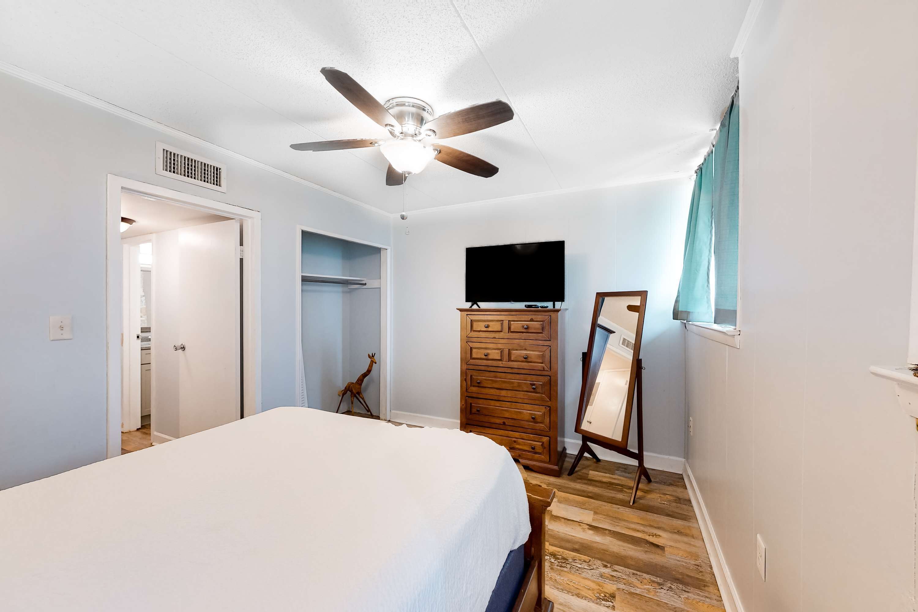 A bedroom with a bed, a ceiling fan, a dresser, a television, and a mirror.