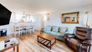 Ein Wohnzimmer mit einer braunen Ledersofa, einem Holztisch, einem hellblauen Sofa und einem Essbereich mit weißen Stühlen und einem Tisch.