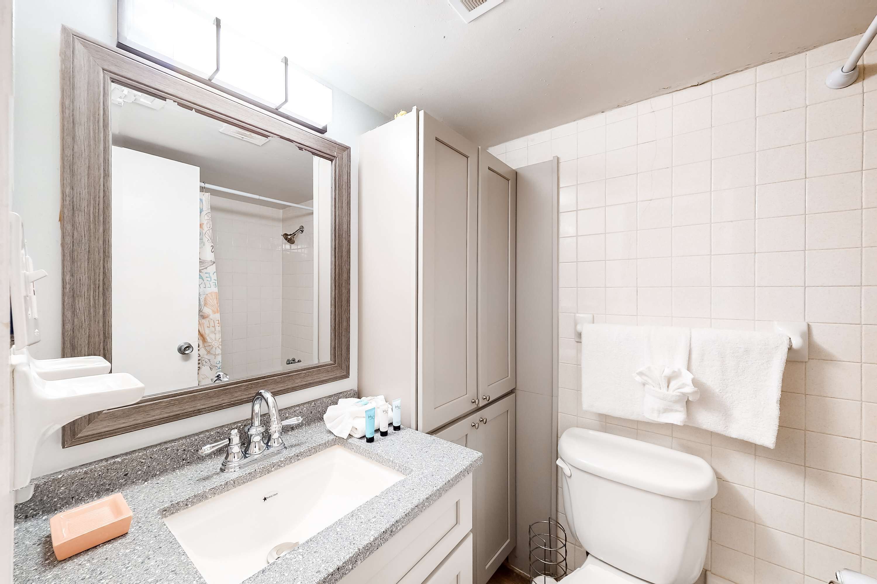 Un baño con lavamanos, espejo, armarios y retrete.