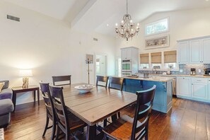 A spacious dining area with a wooden table and chairs, a chandelier, and a view into the kitchen with white cabinets and a blue island. - Dog-friendly home near the beach with beach gear, gas grill & washer/dryer (St. George Island)