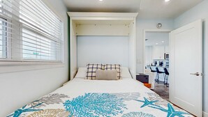 Een slaapkamer met een bed, een raam met zonwering, een deur en uitzicht op een keuken.