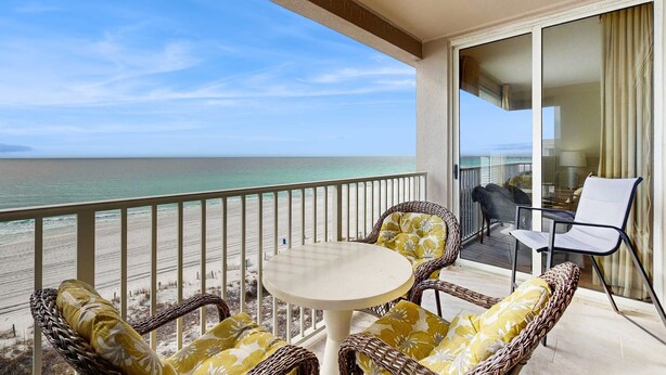 Ein Balkon mit Korbmöbeln und einem Tisch, der Blick auf einen Strand und den Ozean bietet.