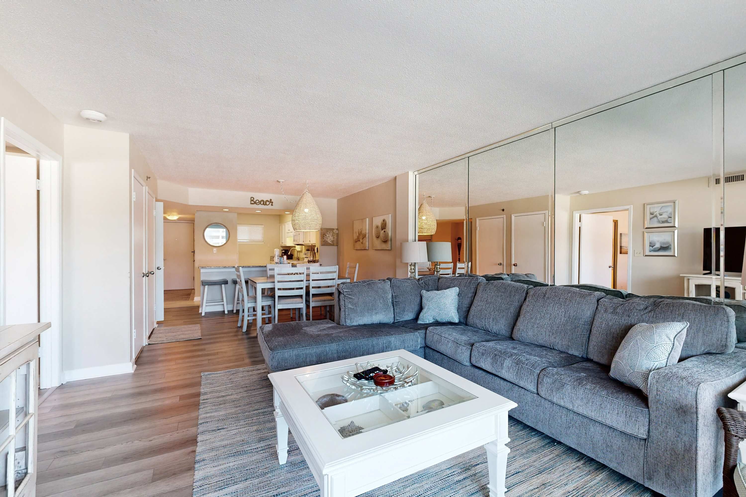 Una sala de estar moderna con un sofá seccional gris, una mesa de centro de vidrio y una zona de comedor al fondo.