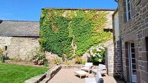 Ein Steinhäuschen mit Garten-Terrasse, Sitzgelegenheiten im Freien und einer mit Efeu bewachsenen Mauer.