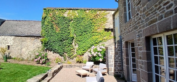 Ein Steinhäuschen mit Garten-Terrasse, Sitzgelegenheiten im Freien und einer mit Efeu bewachsenen Mauer.