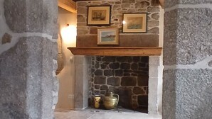 Ein steiner Torbogen führt zu einer Kamin-Ecke mit Steinwänden und Holzbalken.