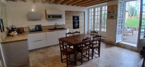 Eine Küche mit Holzesstisch und -stühlen, einem eingebauten Backofen und einem großen Fenster mit Blick zum Garten.