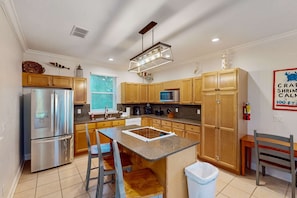 A modern kitchen with wooden cabinets, stainless steel appliances, a central island with stools, and a hanging light fixture. - Renovated dog-friendly home with private pool & spacious decks - near the beach (St. George Island)