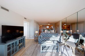 Sala de estar con televisor, sofá y sillones. Se observa una cocina al fondo.