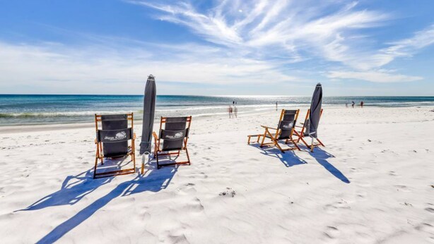 A beach with two beach chairs and a surfboard on the sand. - Sea Oats 708 - 7th floor condo in beachfront complex with pool, Gulf view, W&D, & fast WiFi (Fort Walton Beach)
