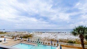 A pool area with lounge chairs and umbrellas, overlooking a beach with a wooden pier. - Sea Oats 708 - 7th floor condo in beachfront complex with pool, Gulf view, W&D, & fast WiFi (Fort Walton Beach)