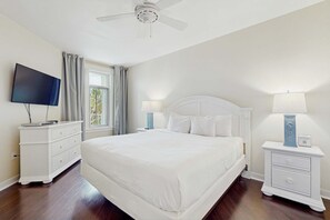 Ein Schlafzimmer mit einem großen Bett, einem Fernseher, einem Deckenventilator und einem Fenster mit Vorhängen.