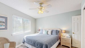 Ein Schlafzimmer mit Bett, Deckenventilator, Nachttisch, Sessel und Tür.