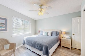 A bedroom with a bed, a ceiling fan, a nightstand, a chair, and a door. - Coastal condo with a pool, patio, washer&dryer, & central AC - easy beach access (Miramar Beach)