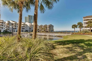 A beachfront hotel with multiple-story buildings, palm trees, and a clear view of the ocean. - Condo with partial bay view, onsite fishing dock, beach access, & shared pool (Pensacola Beach)