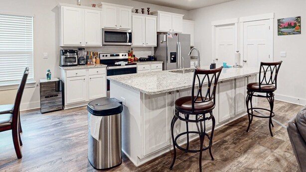 A modern kitchen with white cabinets, stainless steel appliances, a granite countertop, and a bar area with stools. - Gorgeous coastal home with plenty of space, close to everything - dog friendly (Gulf Breeze)
