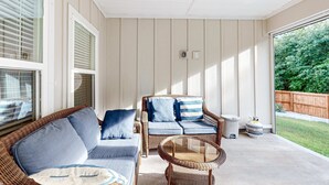 A covered patio with wicker furniture, a glass table, and a view of a wooden fence and greenery. - Gorgeous coastal home with plenty of space, close to everything - dog friendly (Gulf Breeze)