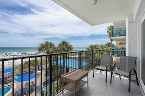 A balcony with wicker furniture, a pool, and a view of the beach and ocean. - Beachfront, 3rd-floor condo with pool, hot tub, ocean view & fast WiFi (Fort Walton Beach)