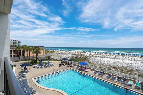 A pool area with lounge chairs and umbrellas, a beach with umbrellas and lounge chairs, and a building in the background. - Beachfront, 3rd-floor condo with pool, hot tub, ocean view & fast WiFi (Fort Walton Beach)