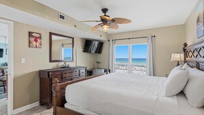 Ein Schlafzimmer mit Bett, Deckenventilator, Fernseher, Schminktisch und Blick auf den Strand.