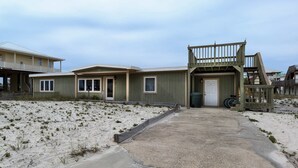 A beachfront building with a sandy beach in front, a wooden deck, and a door leading to the interior. - Dog-friendly beach home with expansive deck, amazing views, & outdoor shower (Pensacola Beach)
