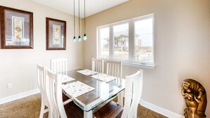 A dining room with a glass table, white chairs, framed botanical prints, and a view through large windows. - Dog-friendly beach home with expansive deck, amazing views, & outdoor shower (Pensacola Beach)