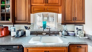 A kitchen with wooden cabinets, a granite countertop, a double sink, and various appliances including a toaster, blender, and coffee maker. - Dog-friendly beach home with expansive deck, amazing views, & outdoor shower (Pensacola Beach)