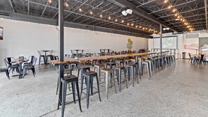 Un espacio interior amplio con una larga mesa de madera y varios taburetes, rodeado de sillas.