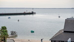 Vista al agua con un muelle que se adentra en aguas tranquilas, una pequeña embarcación amarrada y un edificio con techo inclinado.