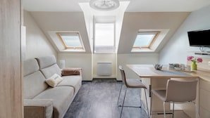 Un dormitorio tipo buhardilla, acogedor y bien iluminado, con sofá, mesa de comedor y televisión.