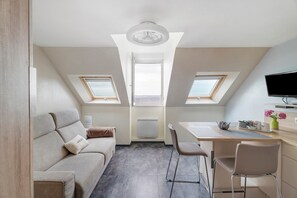 A compact, well-lit attic bedroom with a sofa, a dining table, and a TV. - Duplex Apartment Facing the Sea with Mont Saint Michel View (Cancale)