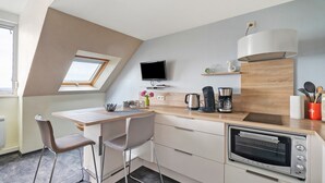 Una cocina moderna con horno empotrado, una zona de comedor con mesa y sillas, un televisor montado en la pared y un tragaluz.