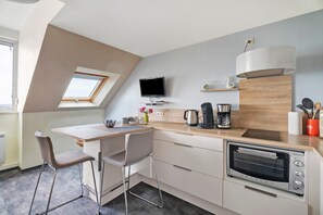 A modern kitchen with a built-in oven, a dining area with a table and chairs, a TV mounted on the wall, and a skylight. - Duplex Apartment Facing the Sea with Mont Saint Michel View (Cancale)