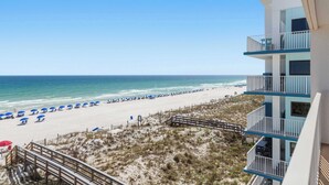 A beach view from a building with multiple balconies, a sandy beach with umbrellas, and a clear sky. - Dreamy island escape with beach access, pool & complimentary seasonal beach service (Fort Walton Beach)