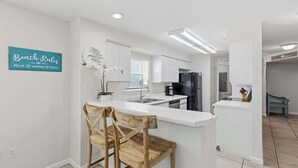 A modern kitchen with white cabinetry, a central island, and a 'Beach Rules' sign. - Dreamy island escape with beach access, pool & complimentary seasonal beach service (Fort Walton Beach)